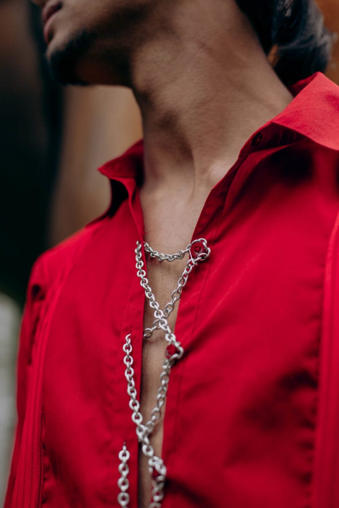 Saad wearing a red shirt fastened by a chain woven through the buttonholes.