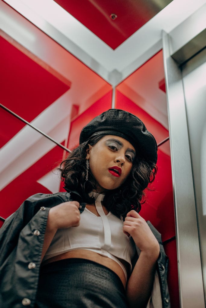 Cherie wearing a black and white outfit with a handmade matching black skirt and beret, in a red glass lift in Canary Wharf