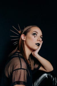 A halloween themed self portrait against a black backdrop with a gold crown and red teardrop facial gems