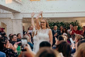 Claudia and Nicole leave their wedding ceremony through gold confetti with a choir behind them