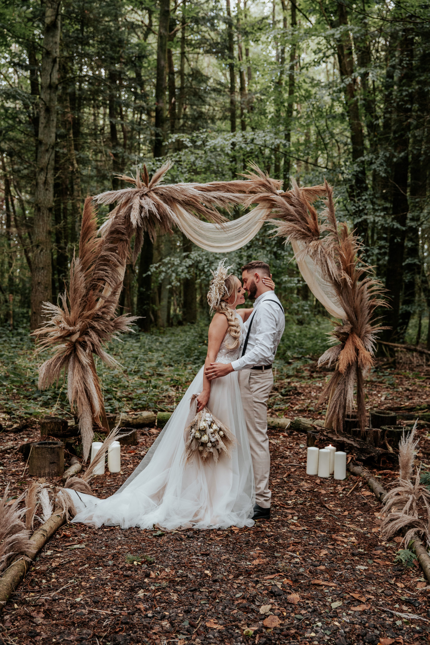 Will and Jess kiss in boho wedding outfits infront of Longton Wood's wooden archway