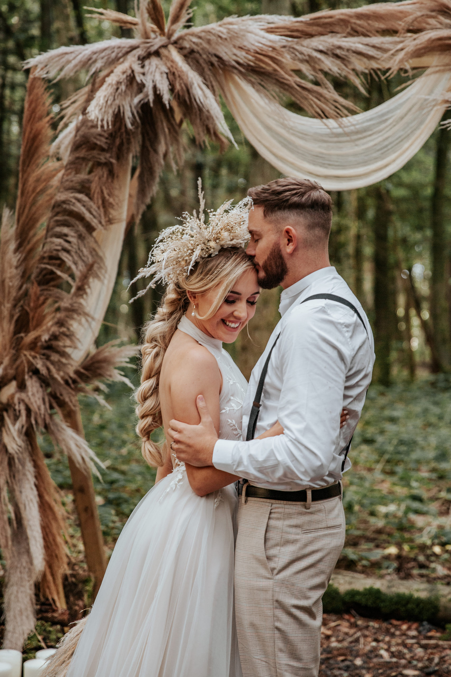 Will and Jess embrace in boho wedding outfits infront of Longton Wood's wooden archway