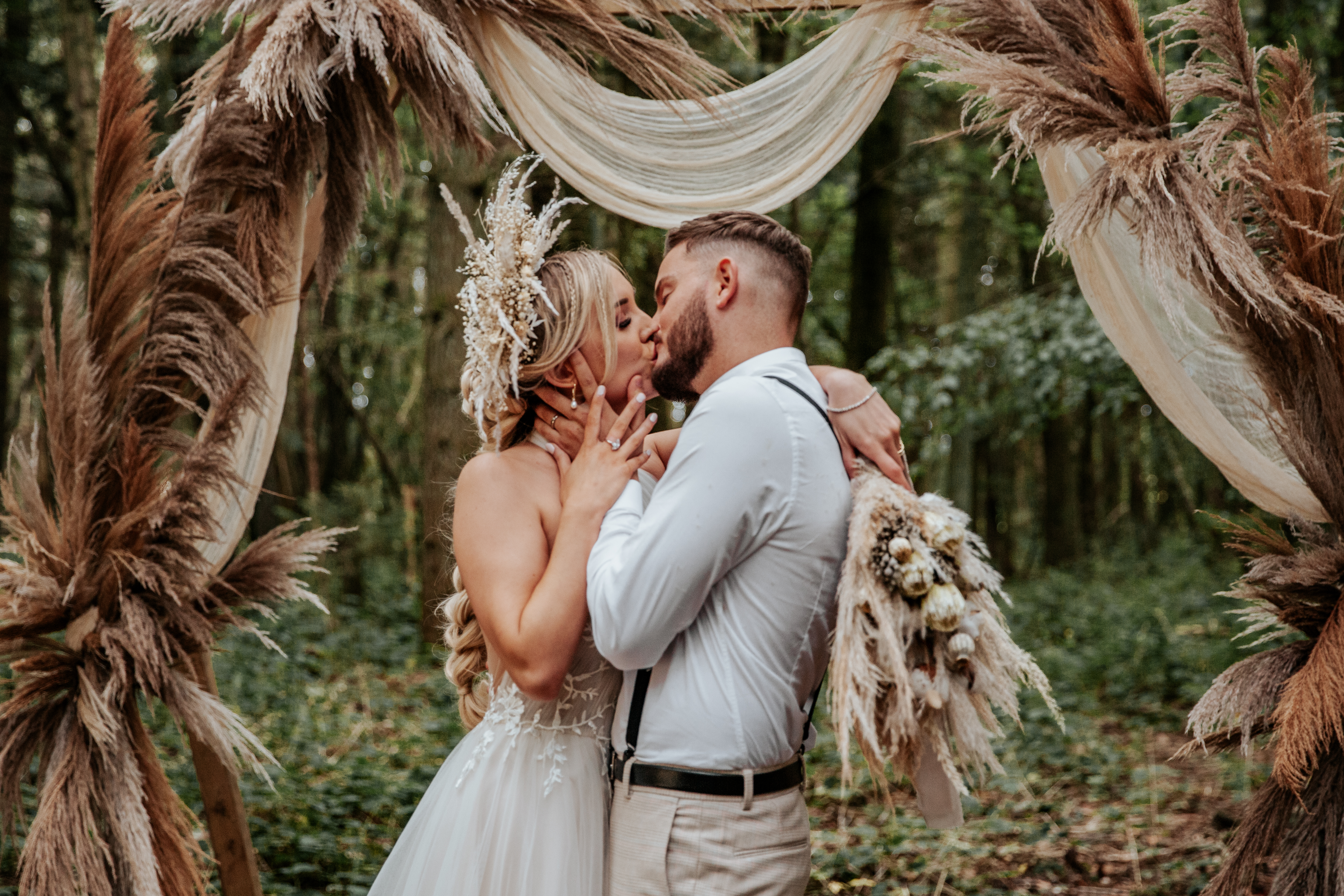 Will and Jess kiss in boho wedding outfits infront of Longton Wood's wooden archway