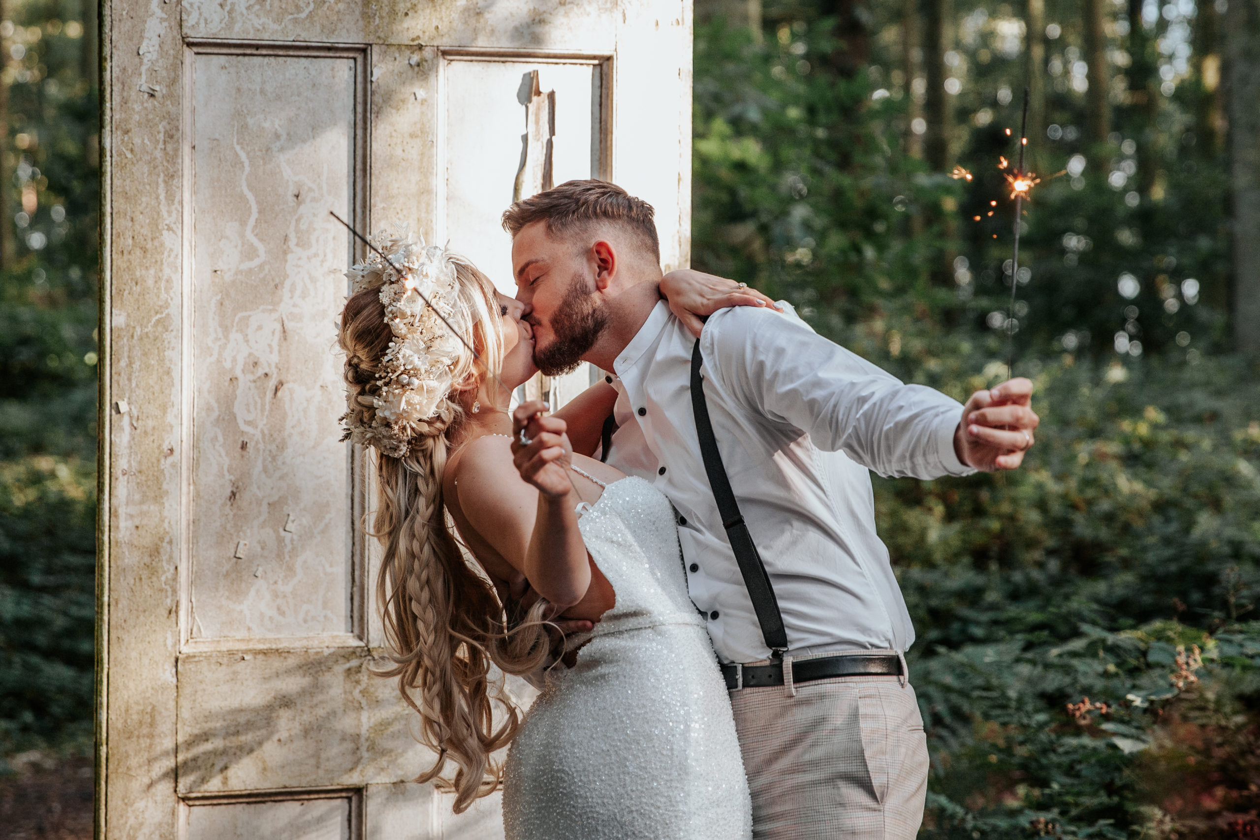Will and Jess kiss while waving sparklers at golden hour infront of Longton Wood's white doors