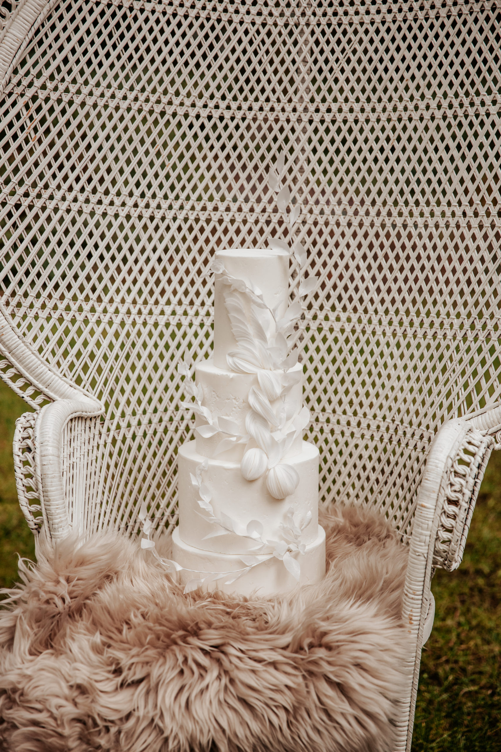 Decorative white cake by Cobi and Coco Cakes, sat on a wicker peacock chair
