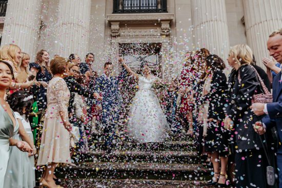 bride and groom walk down the steps of Old Marylebone town hall in a flurry of paper confetti