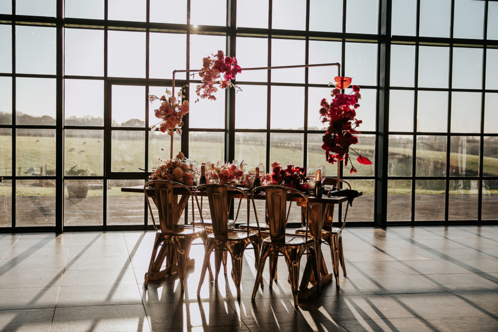 A wedding table set up in botley hill barn, with gold chairs and a gold frame decorated with pink flowers