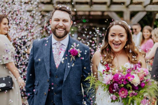 bride and groom walk through pink and white confetti, matching their flowers