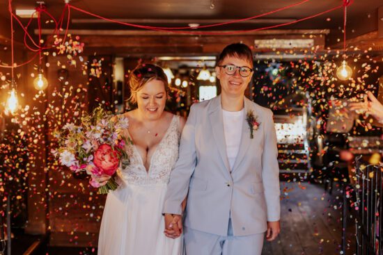 two brides walk through a confetti tunnel inside The Bell in Ticehurst