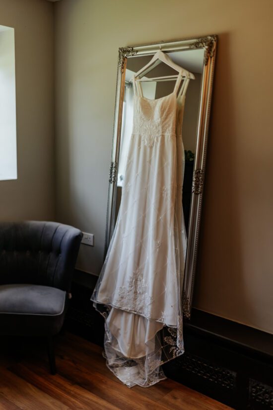 A wedding dress hanging from a tall mirror in a clear bridal prep room