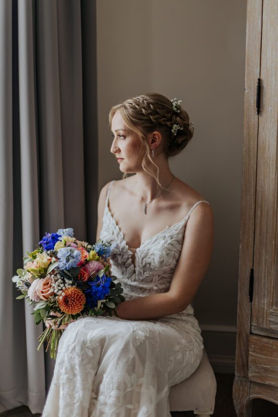 Bride sitting by a window holding her bouquet in the natural light