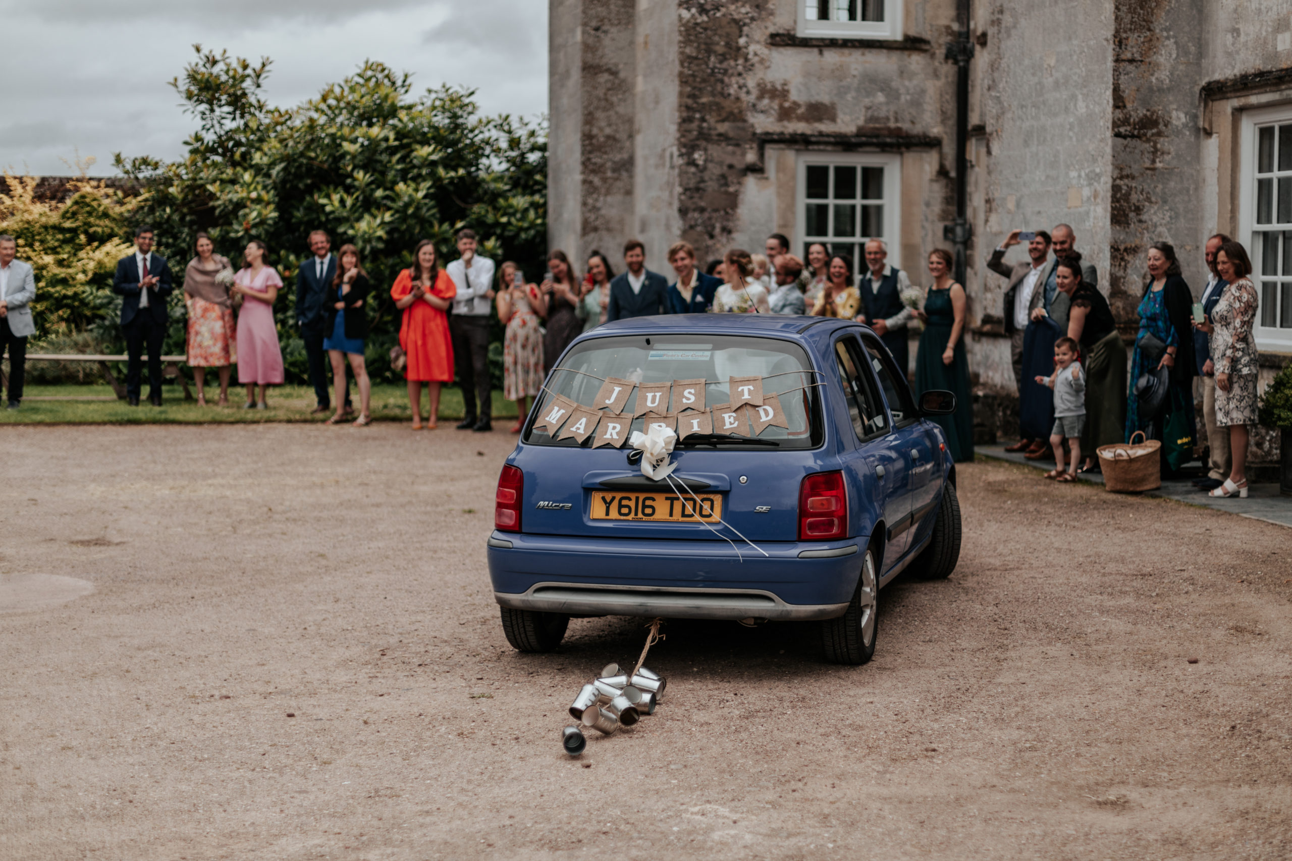 Sarah &amp; Cam&#039;s old Nissan Micra pick them up to take them to their festival wedding reception, with cans tied to the back