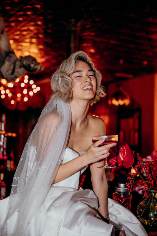 Emma sat on the bar in a club in Shoreditch in a wedding dress and a veil, holding a cocktail