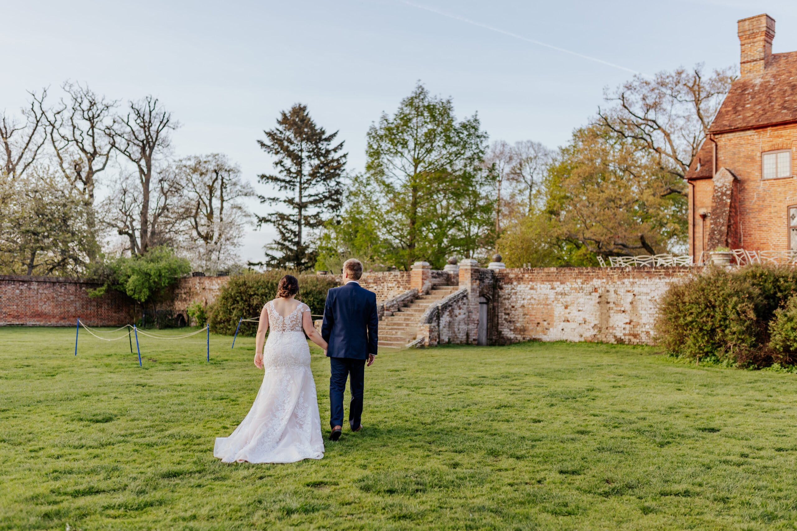 Bride and groom walk away, holding hands in the sunken garden at sunset at Ufton Court
