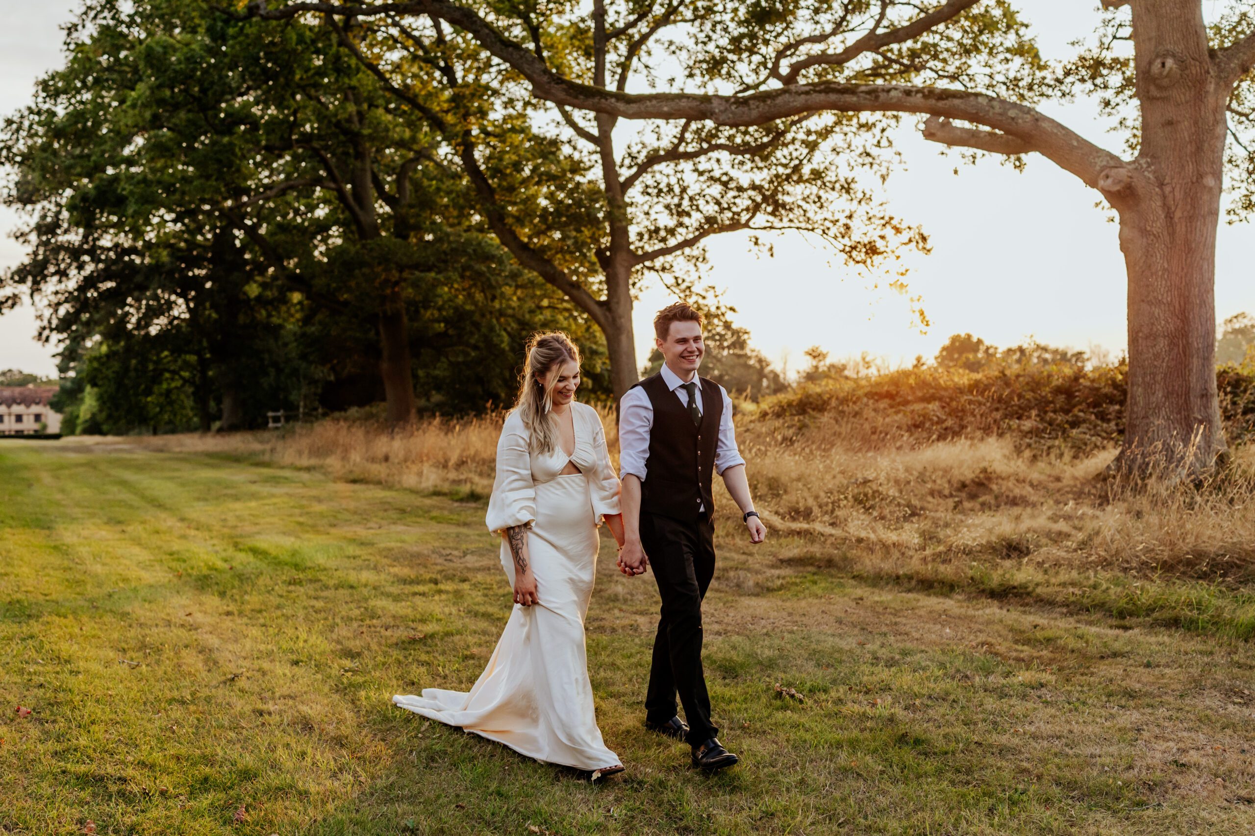 Bride and groom walk across a lawn at Ufton Court during golden hour