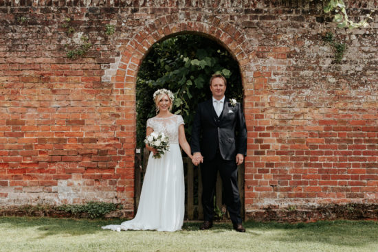 Hannah and Simon stand in a brick archway holding hands