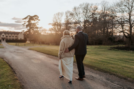 Anna and Rich walk with their backs to the camera towards the Ufton Court manor house at sunset