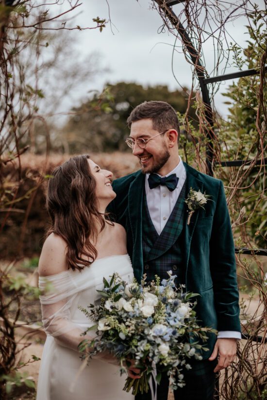 Bride and groom smile at eachother while stood underneath a garden archway in Ufton Court's herb garden
