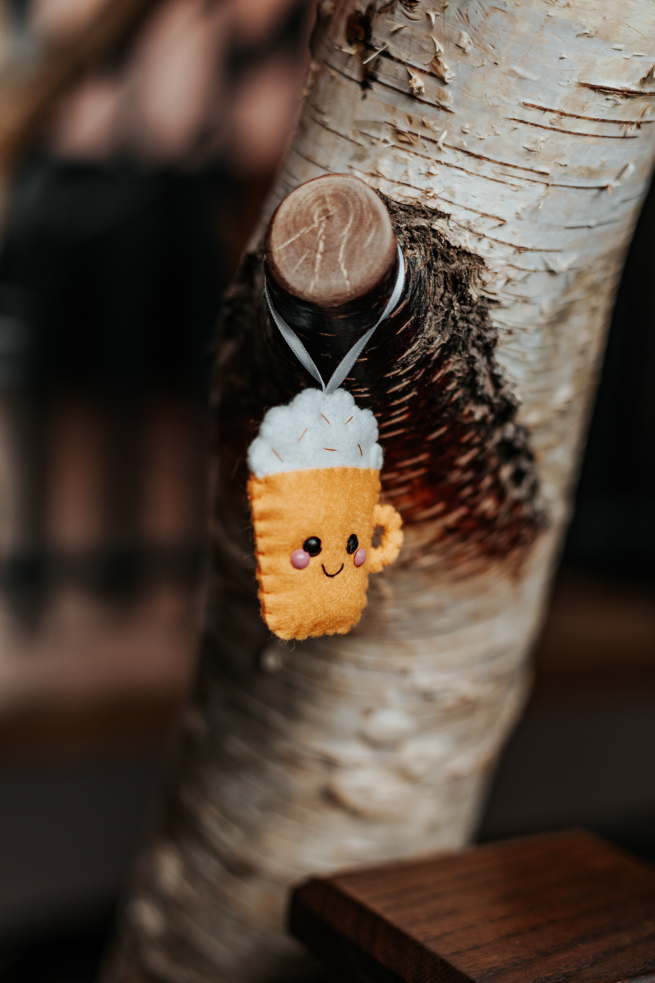 An embroidered pumpkin spiced latte with a smiley face hangs from a tree
