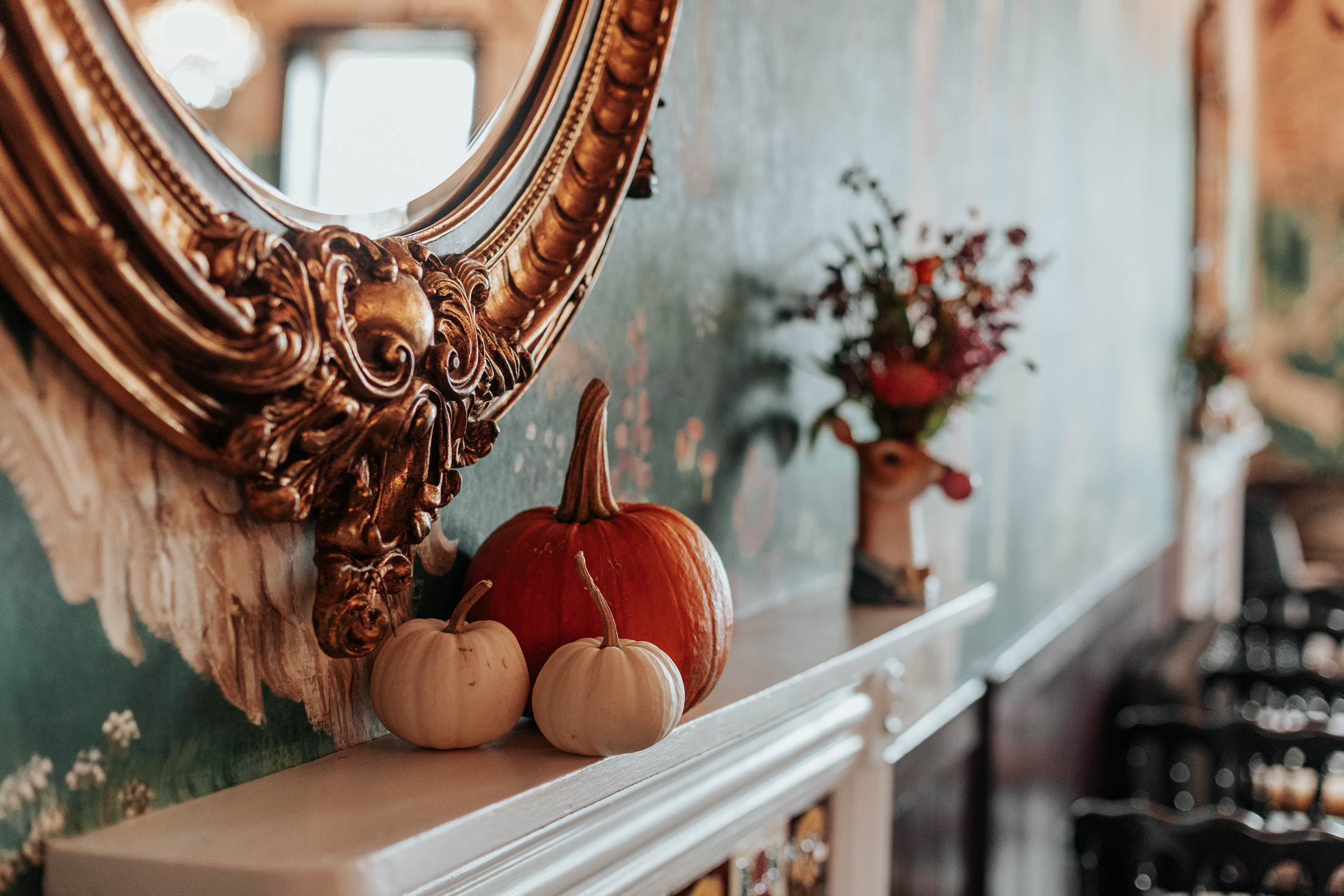 Pumpkins sat on a fireplace, below a gold mirror