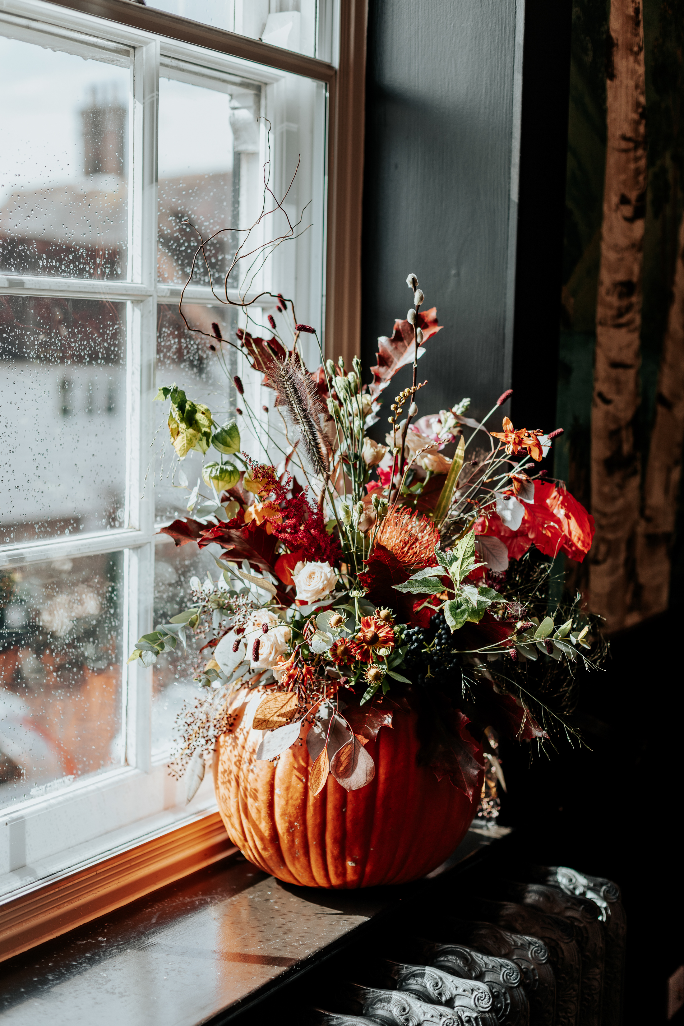 A pumpkin sat on a windowsill, filled with autumnal flowers