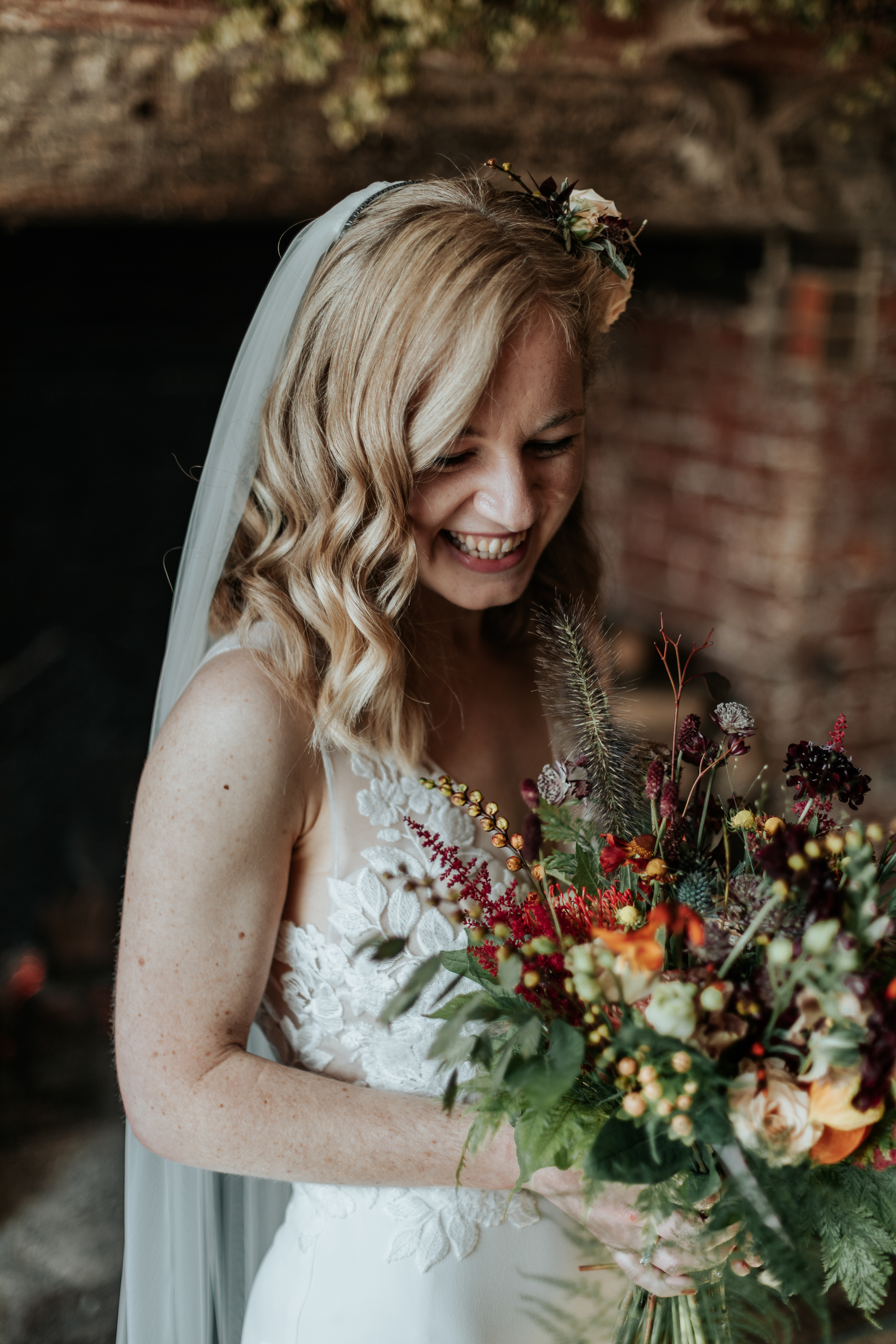 Maddie in her bridal outfit, smiling down at her autumnal wedding bouquet
