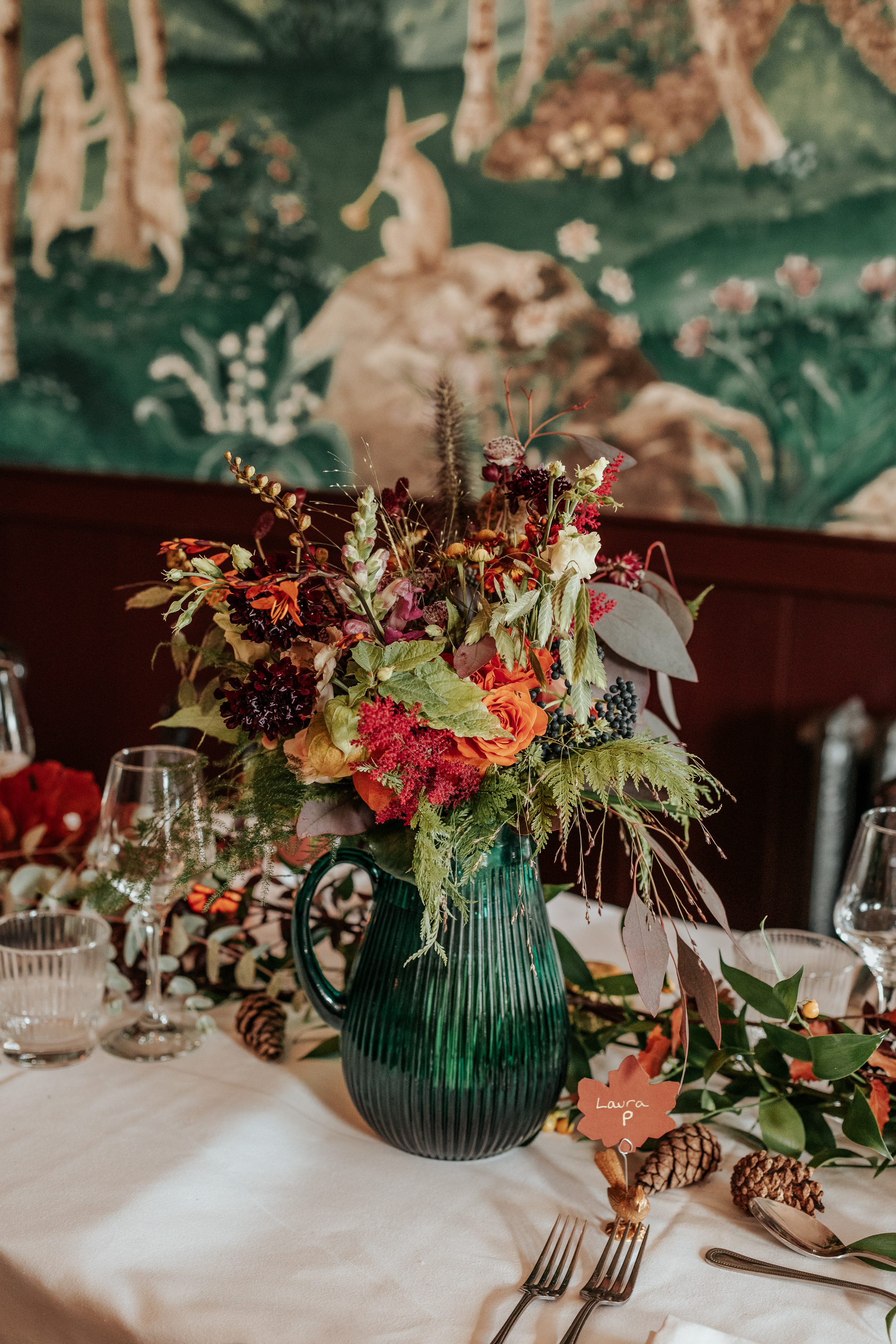 A green vase filled with autumnal flowers, sat on a banquet table