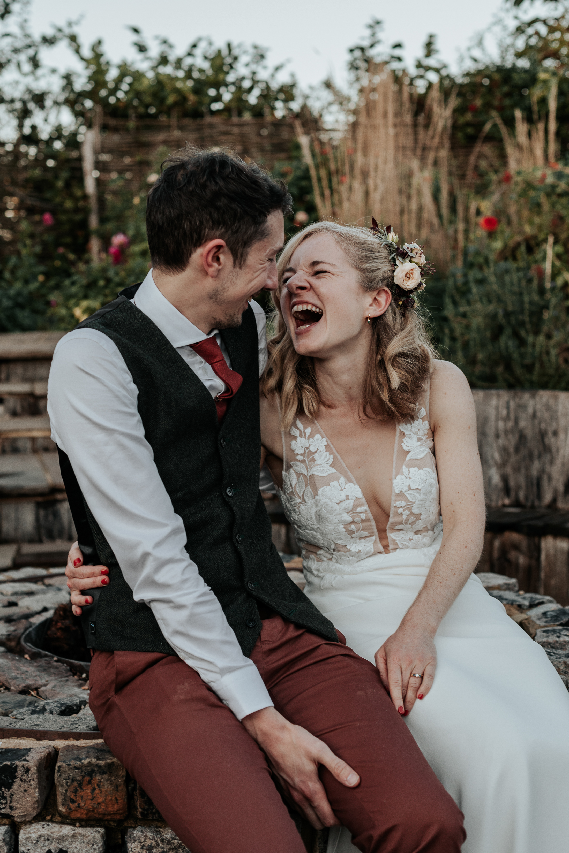 Bride and Groom sit at a firepit together, smiling at eachother