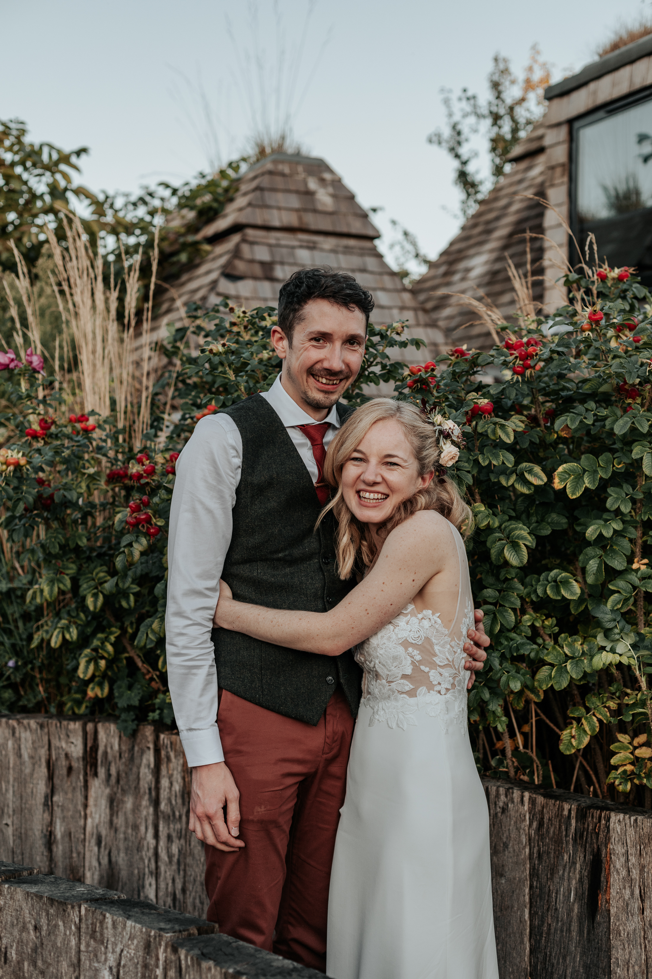 Bride and Groom hold eachother amongst the flowers and greenery, smiling at the camera