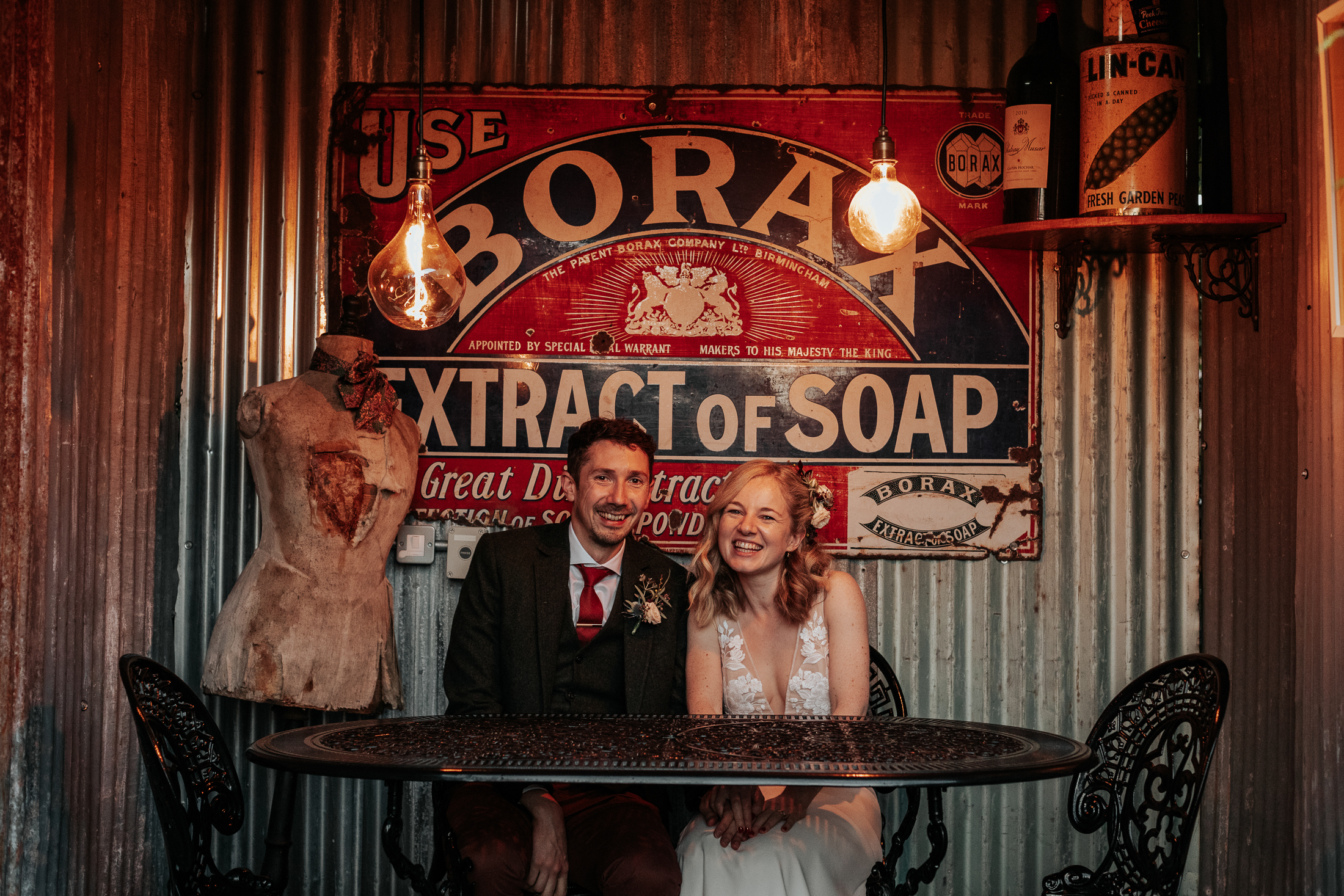 Bride and Groom sit at a table with an iron panel background with filament bulbs hanging above them