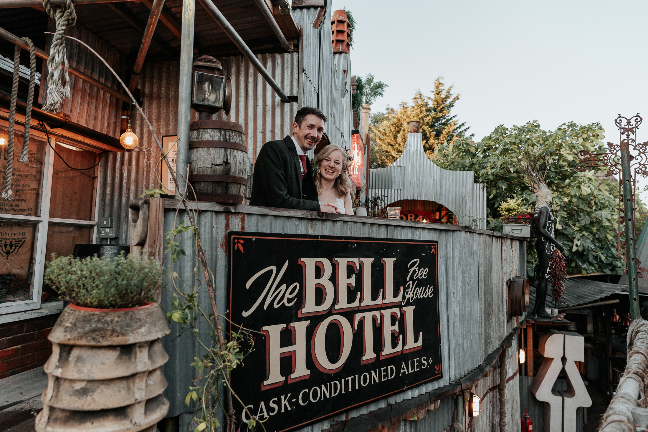 Maddie and Will stand above a sign for The Bell in Ticehurst during their wedding portraits