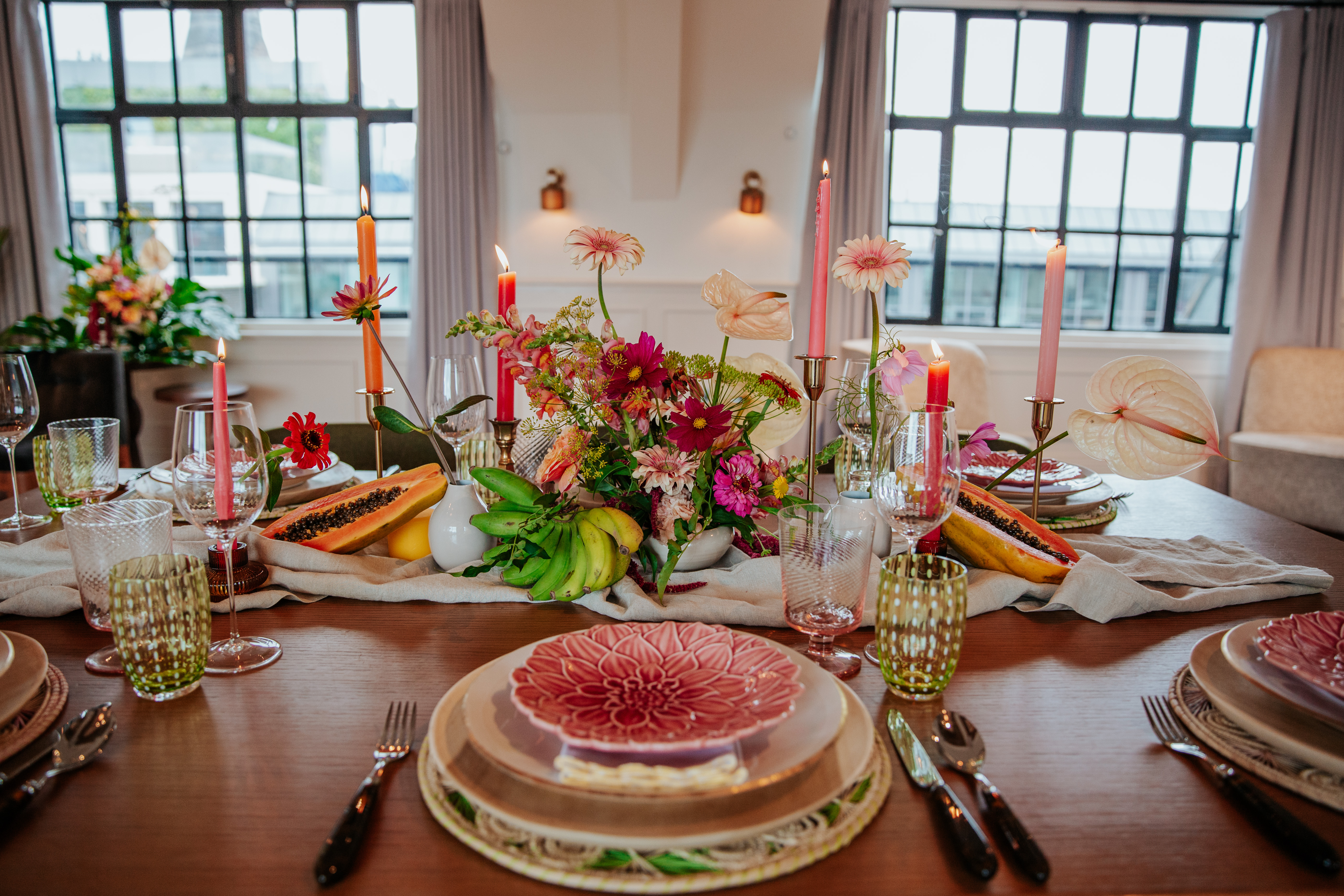 A close up of a table place setting with pink and orange flowers and candles, green chairs, and pink and green tableware