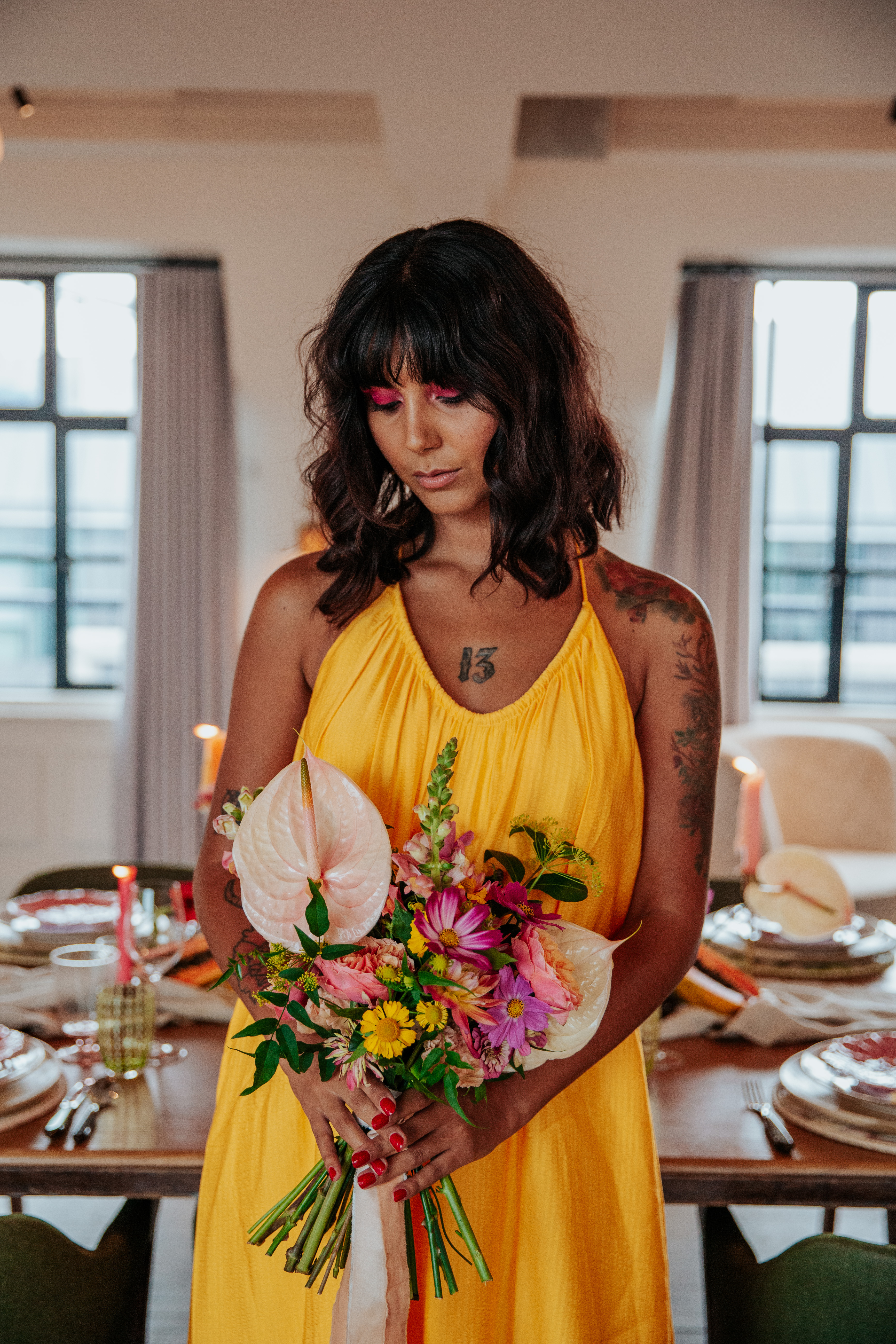 Meera holding a bouquet of tropical coloured flowers while wearing a yellow dress and hot pink eyeshadow