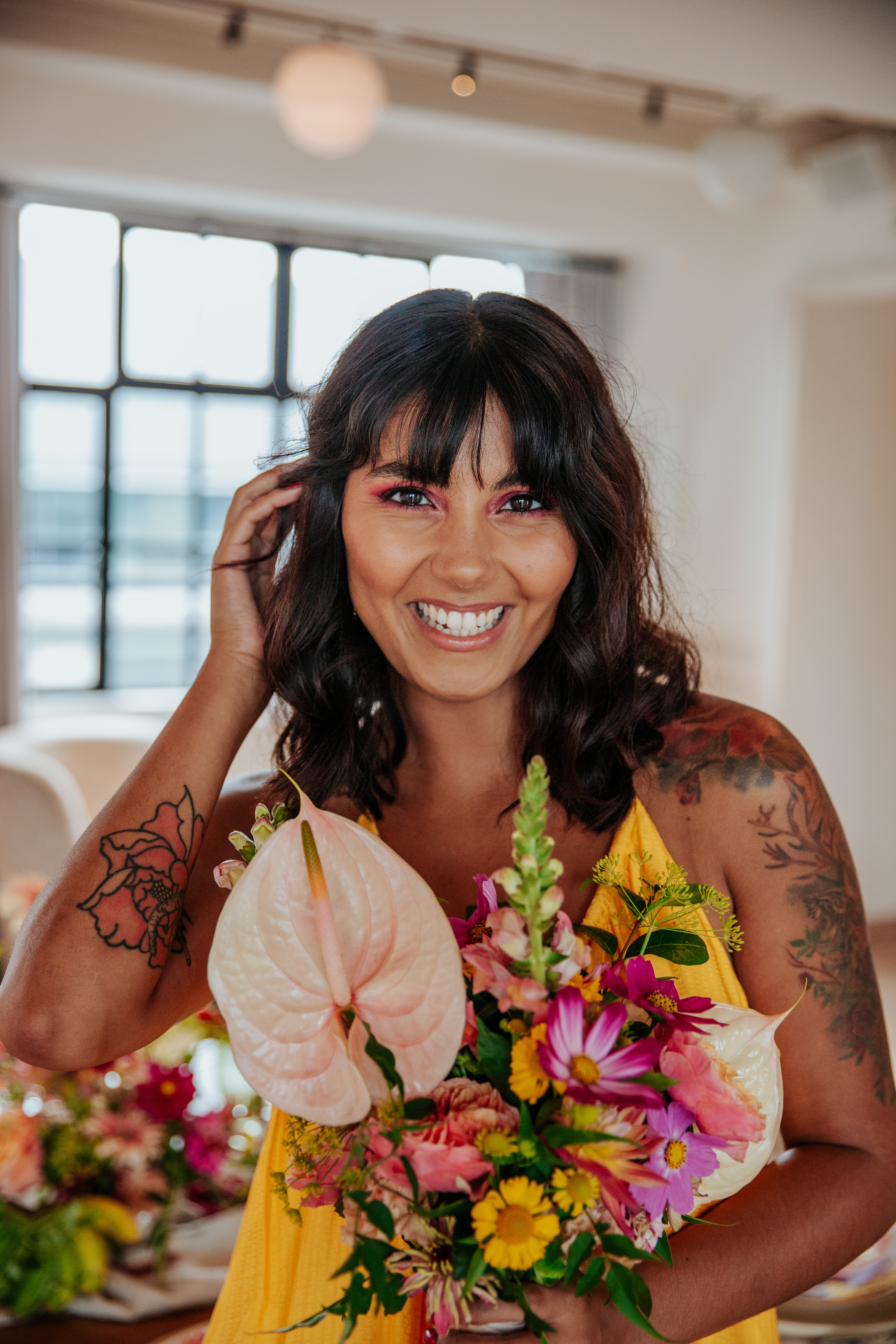 Meera smiles at the camera while holding her bouquet and tucking her hair behind her ear