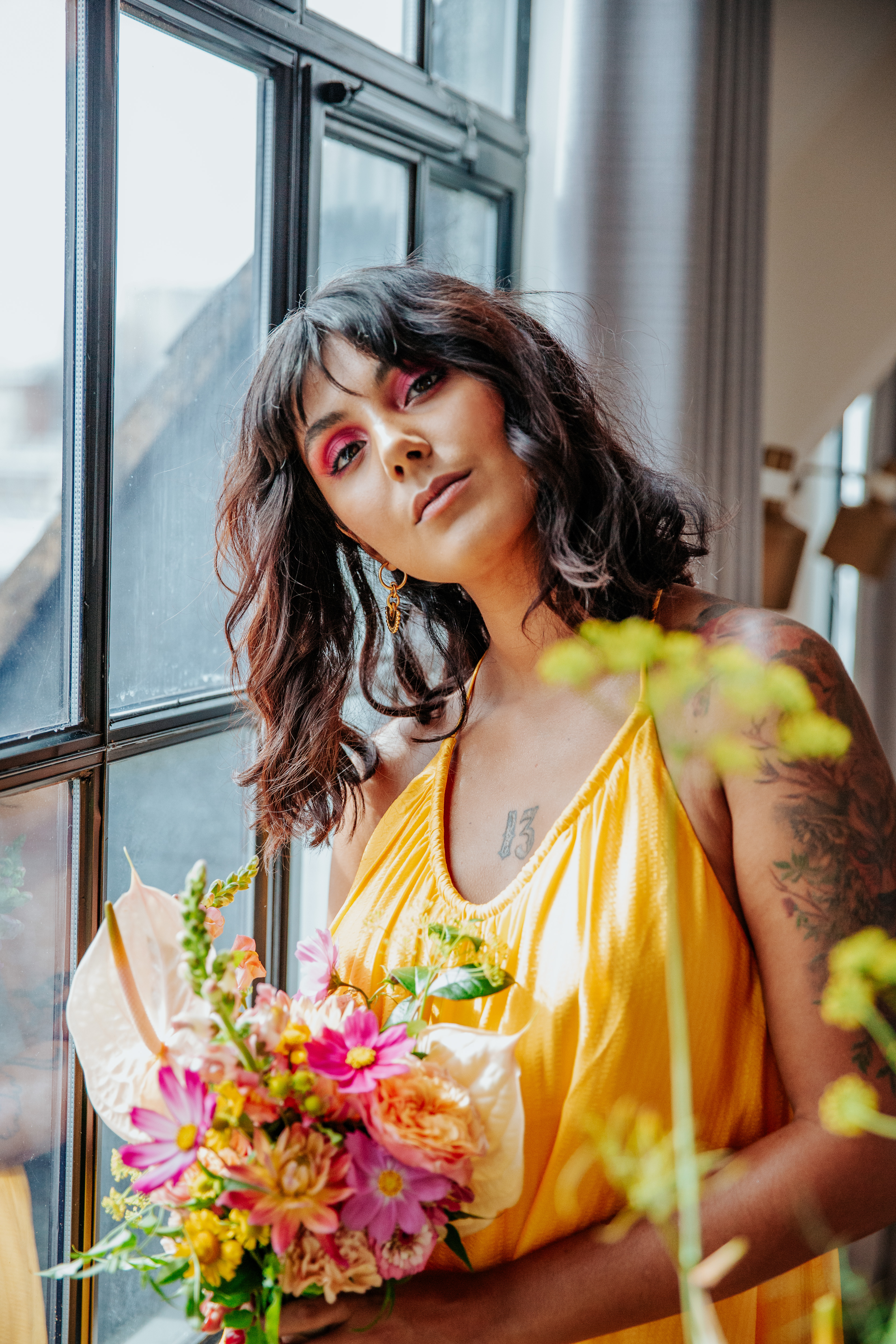 Meera leans against the large windows of Mortimer House's gallery, holding her bouquet