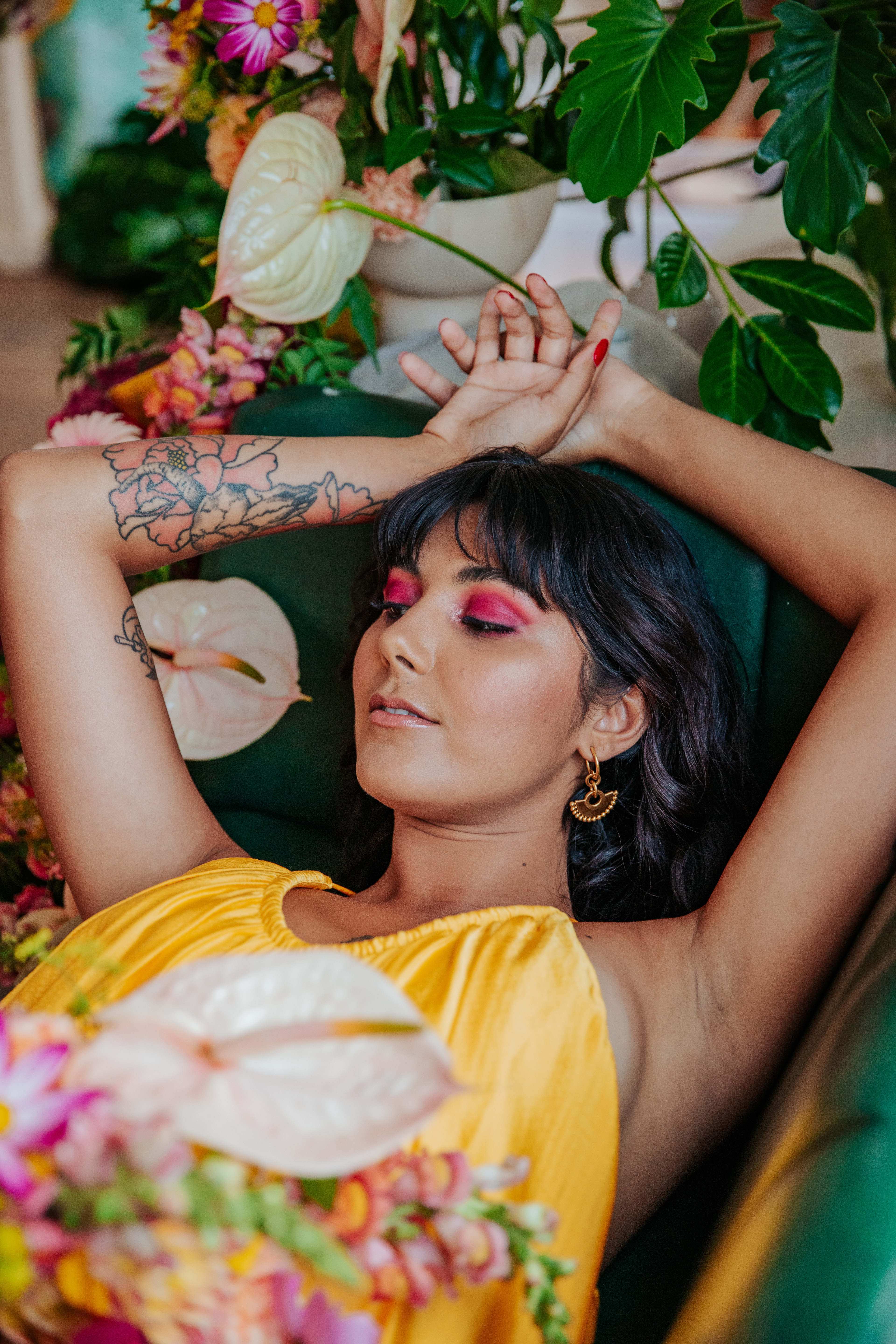 Meera lounges on a green leather booth, holding her bouquet next to a tropical floral display