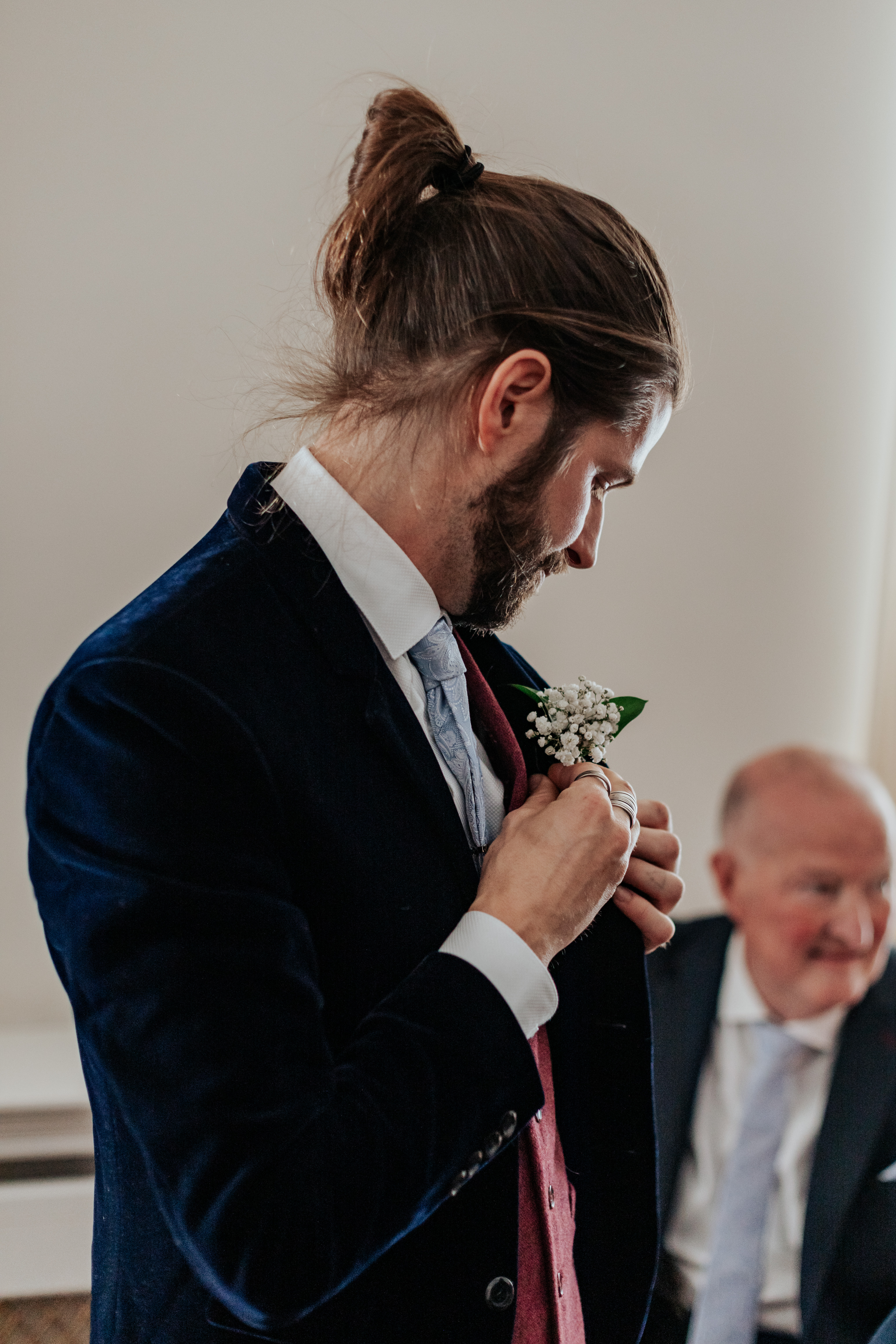 HannahSam25_07-017 Groom puts on his buttonhole in his mix-and-match suit in the Edwardian Room at Woowich Town Hall