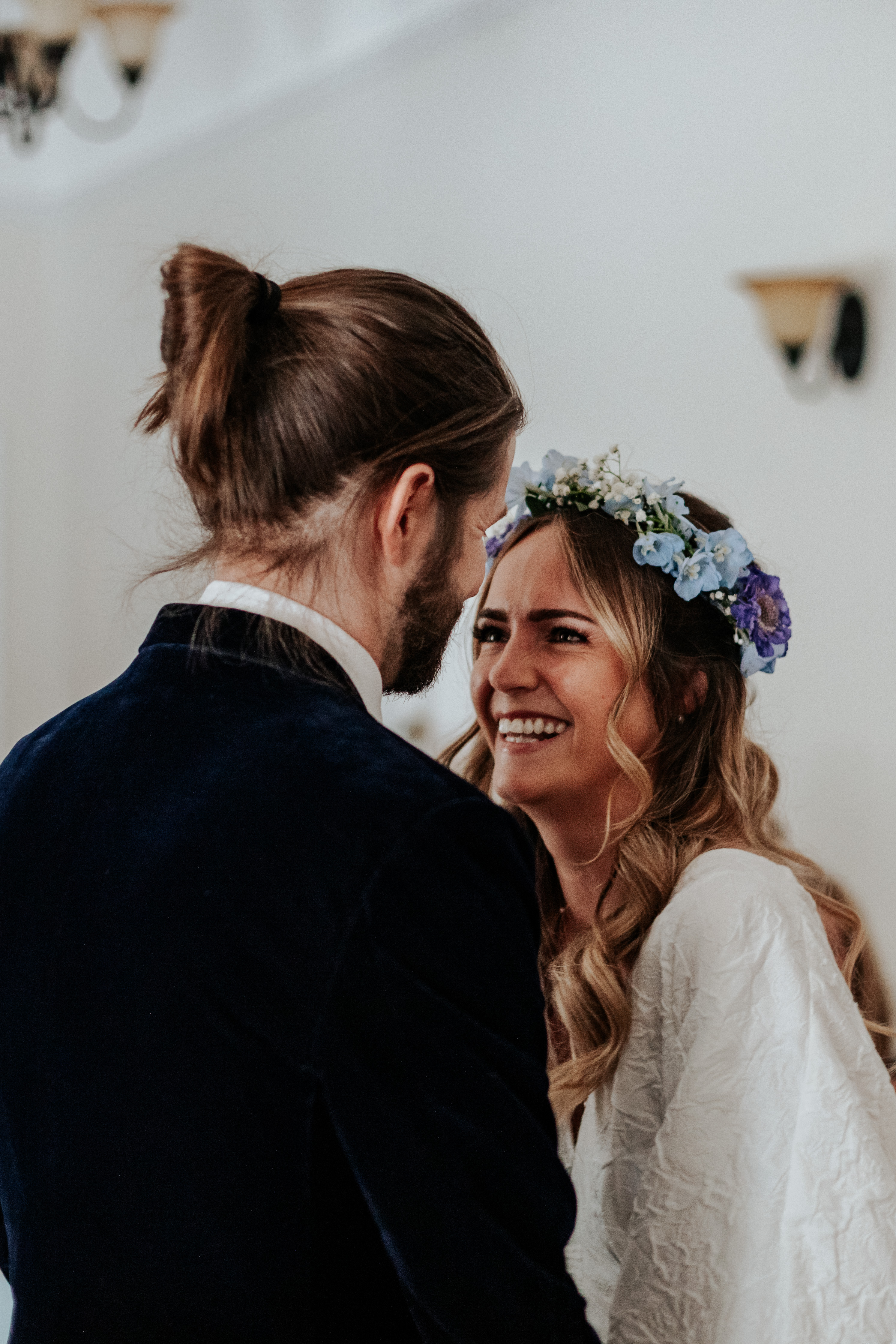 HannahSam25_07-047 Bride smiles at her groom, wearing a blue flower crown and white boho dress