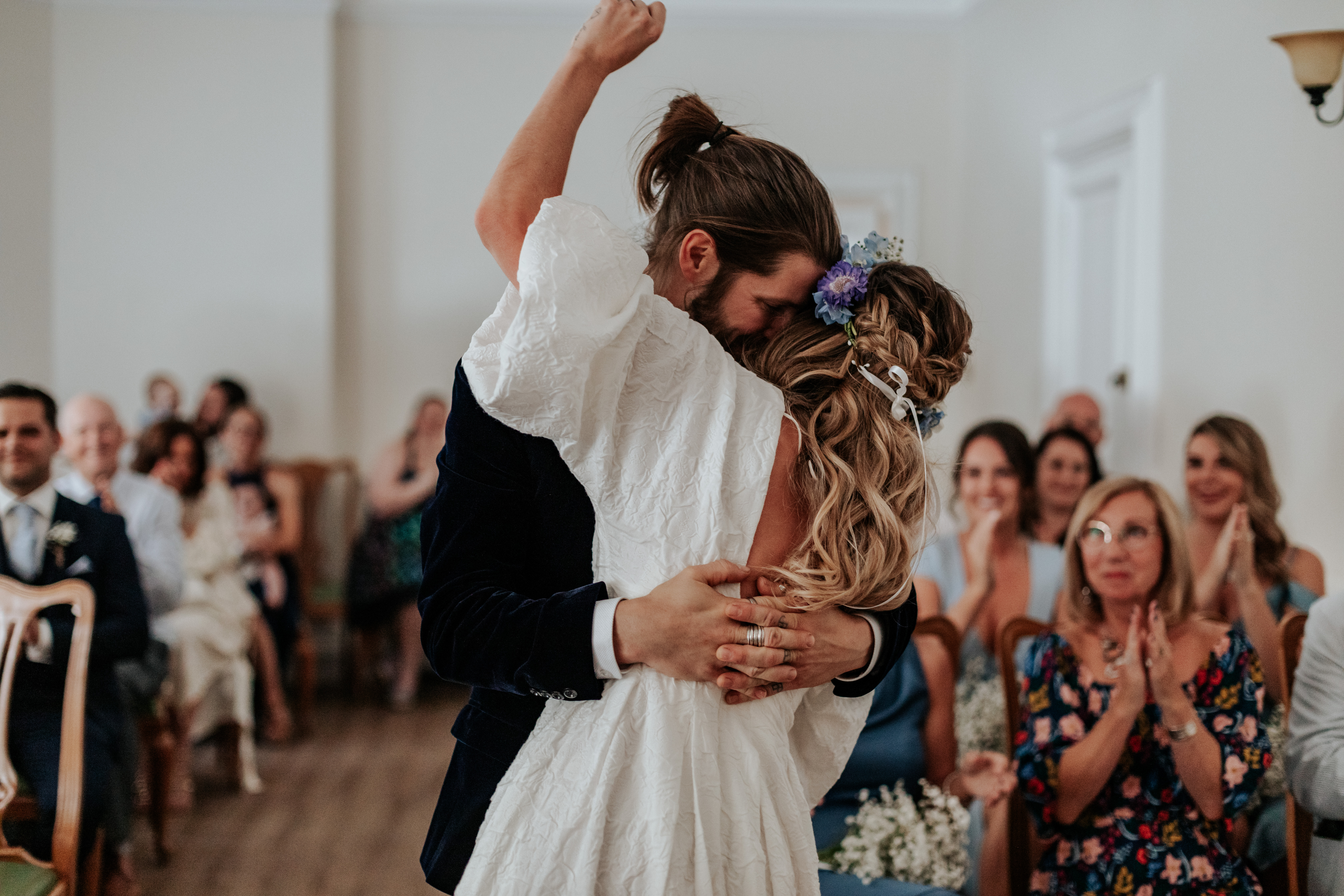 HannahSam25_07-076 Bride and groom kiss with bride's fist in the air while the crowd claps and whistles in the background