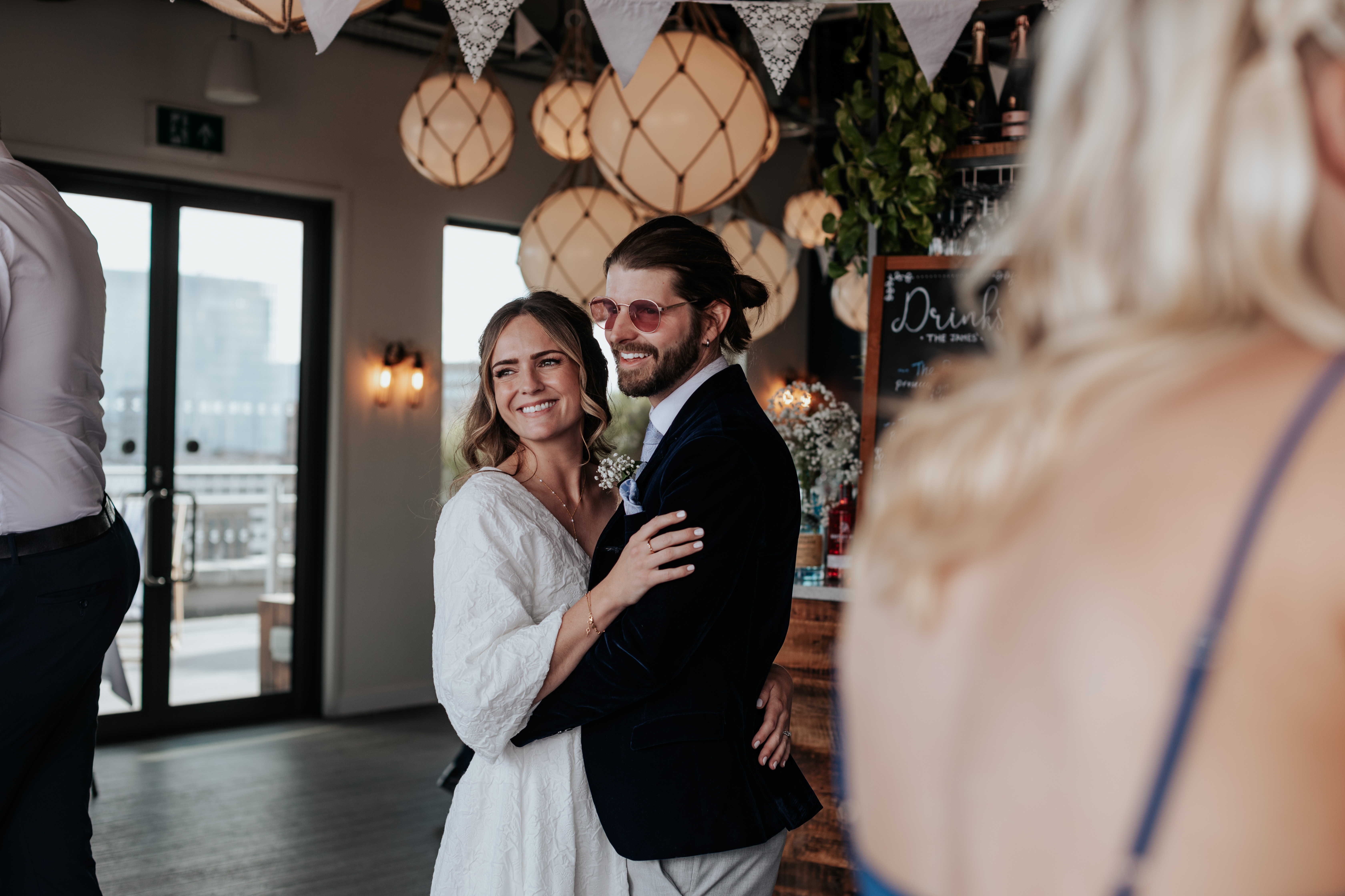 HannahSam25_07-311 Bride and groom embrace while smiling at a guest during their London wedding reception