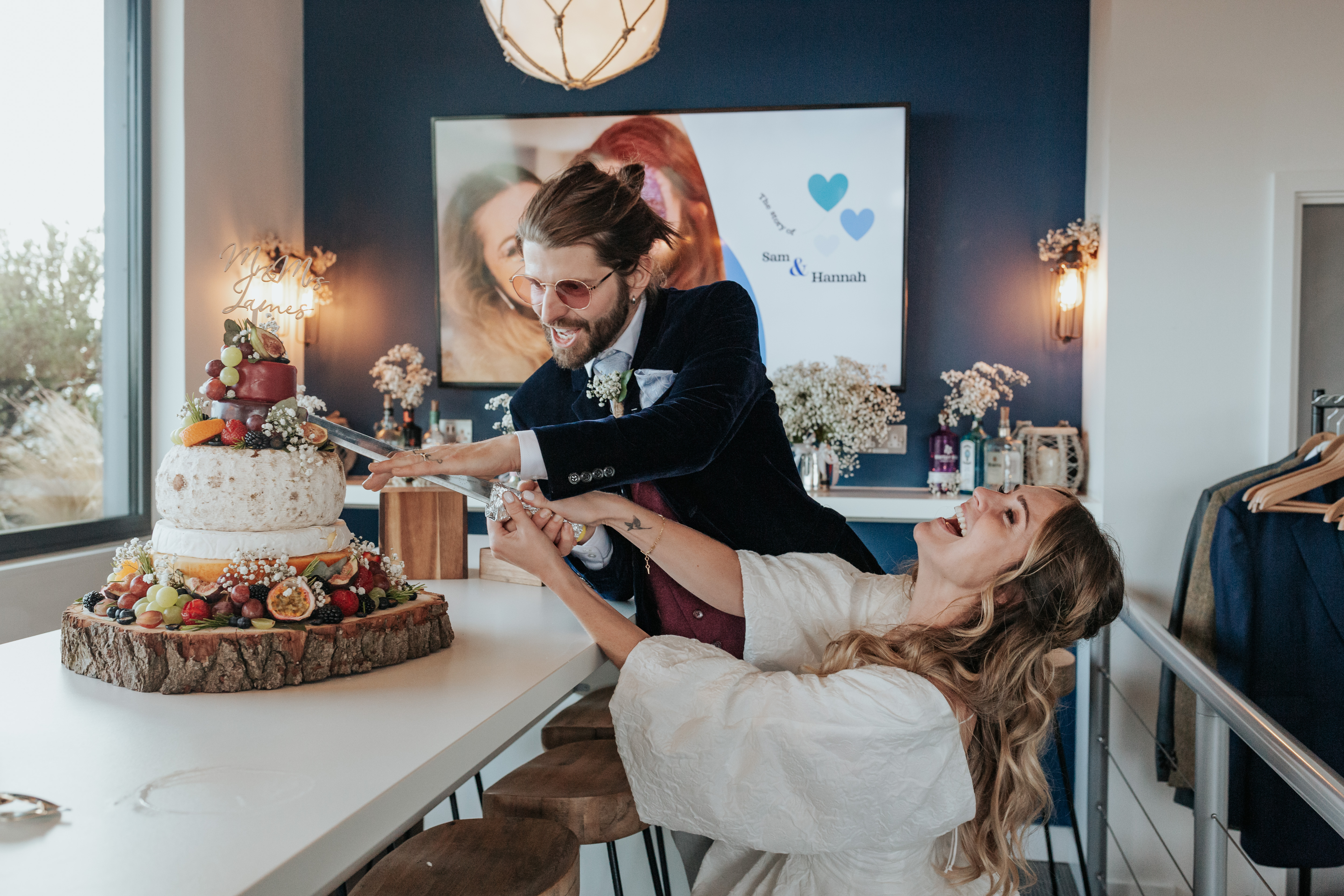 HannahSam25_07-443 Bride and groom struggling to cut their cheese wedding cake
