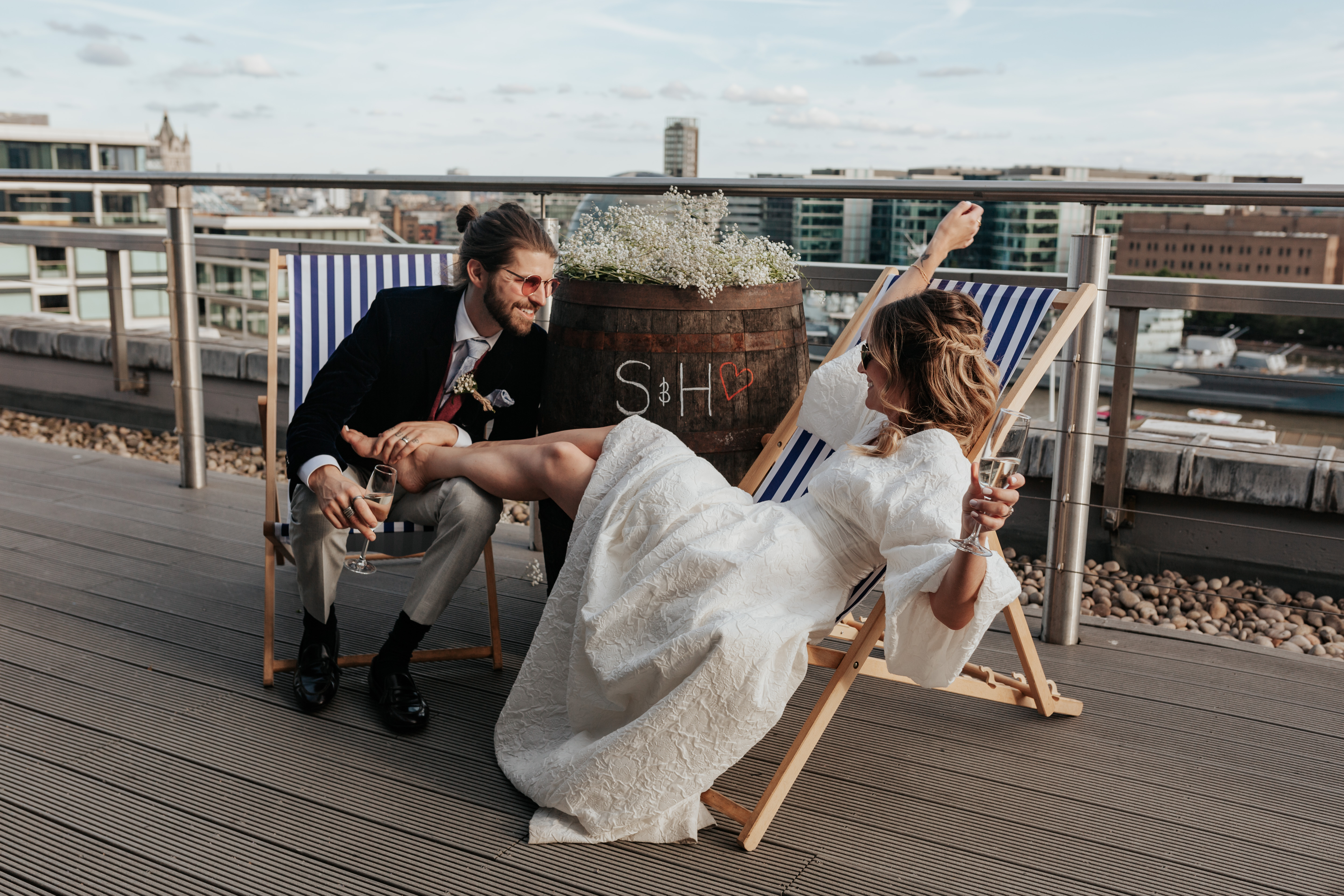HannahSam25_07-450 Bride and groom lounge together in deck chairs on the rooftop terrace of a London bar
