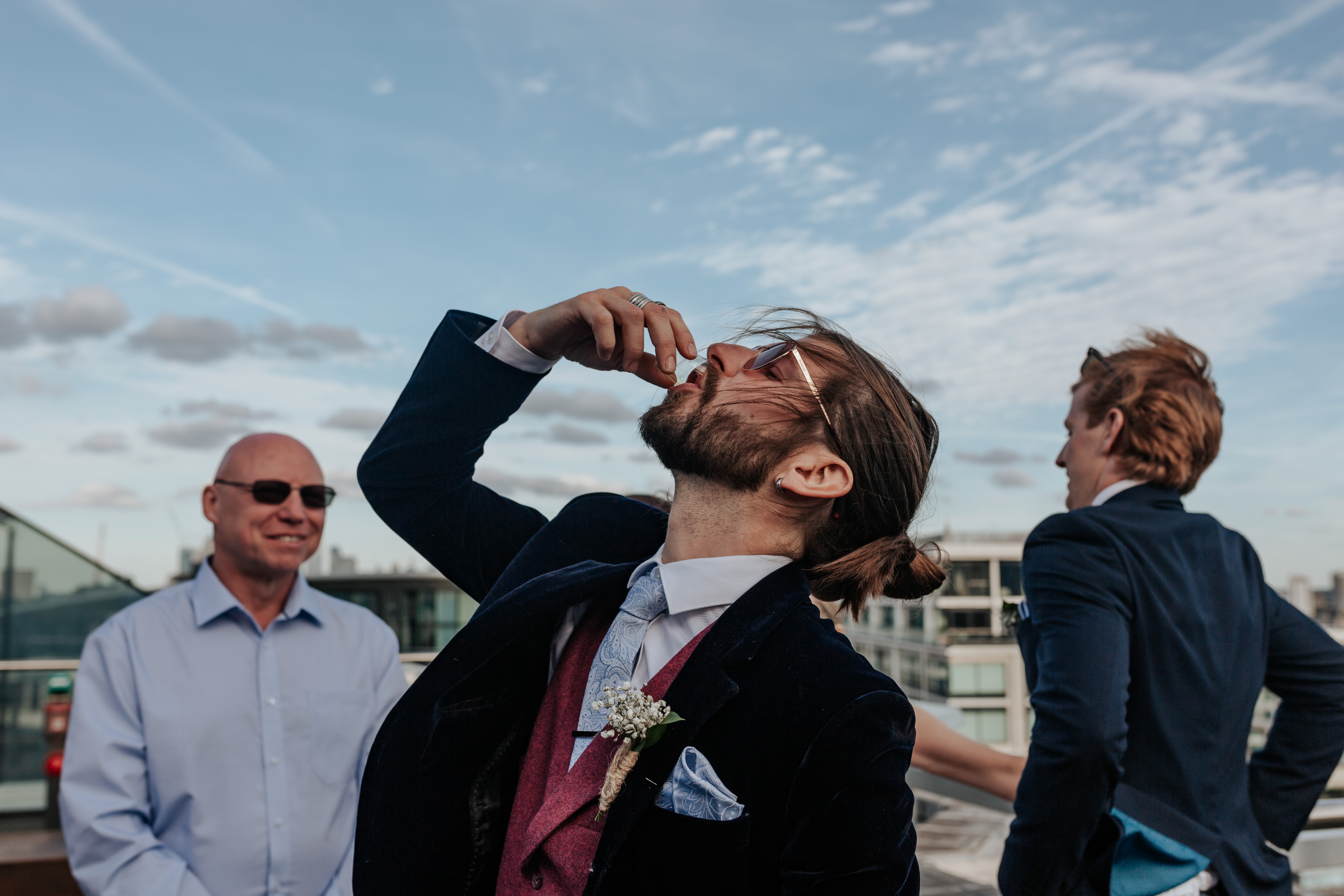 HannahSam25_07-457 The groom takes a shot during his wedding reception Bride and groom lounge together in deck chairs on the rooftop terrace of a London bar