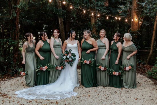 Bride and bridesmaids wearing multiway dresses in different shades of green under festoon lights
