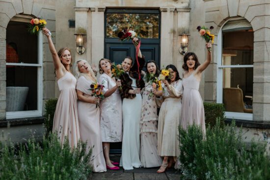 Bride and bridesmaids pose outside a front door wearing different light pink dresses