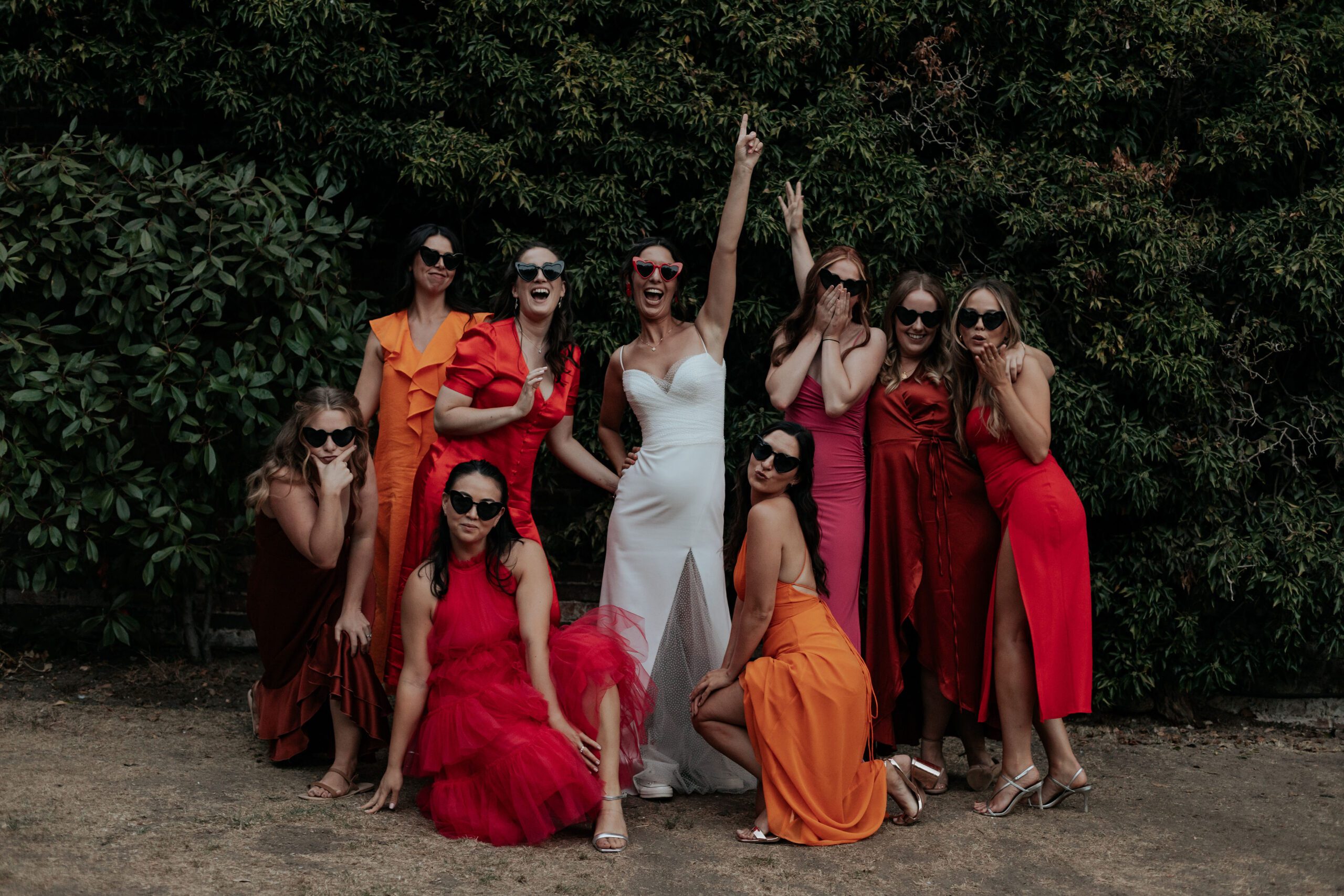 Bride and bridesmaids strike a pose wearing heart shaped sunglasses and mismatched bridesmaid dresses