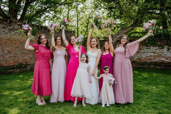 Bride and her bridesmaids holding their bouquets in the air, all wearing different pink dresses
