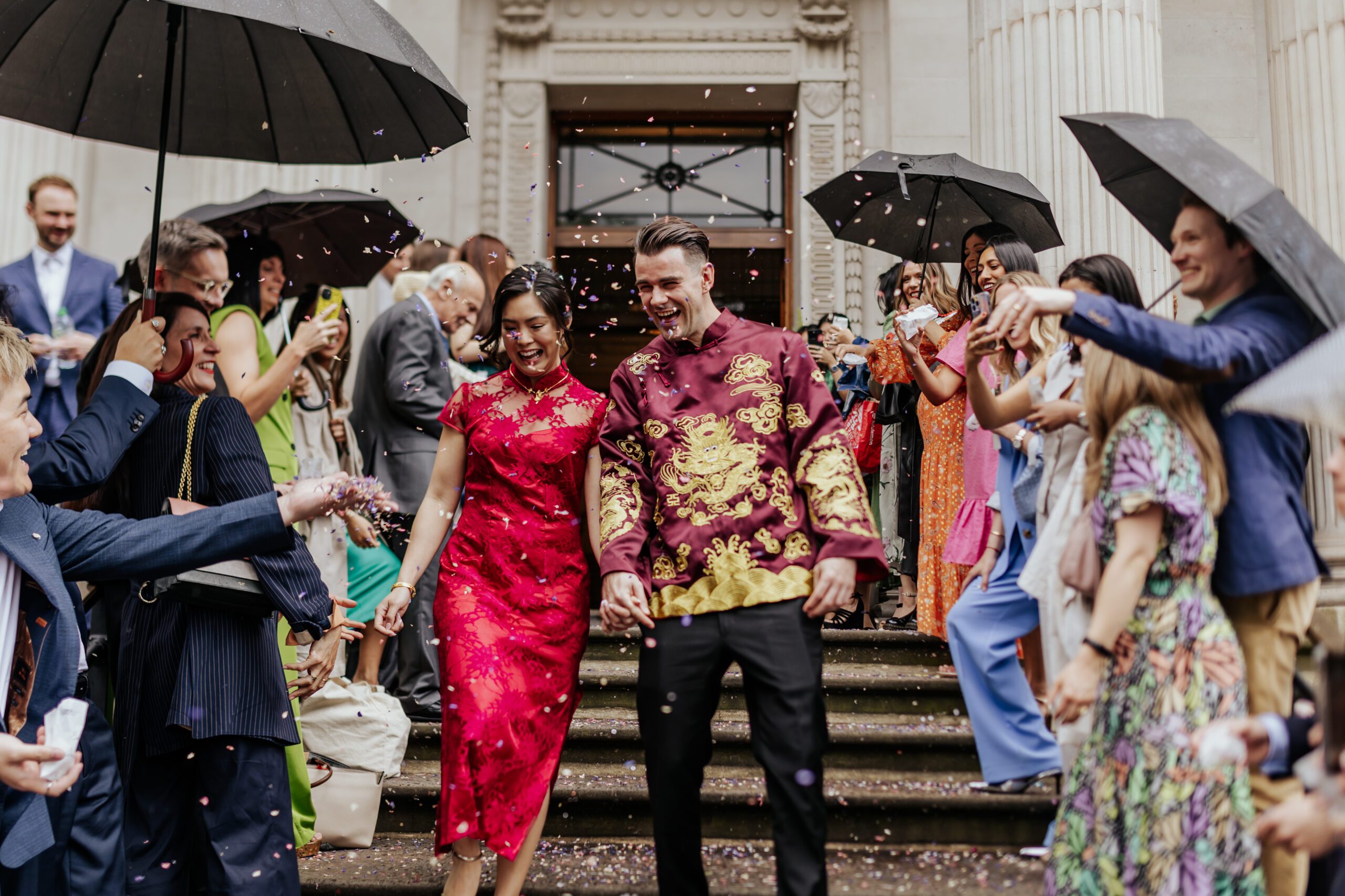 Newlyweds at their chinese wedding walk through a confetti tunnel in the rain at Old Marylebone Town Hall