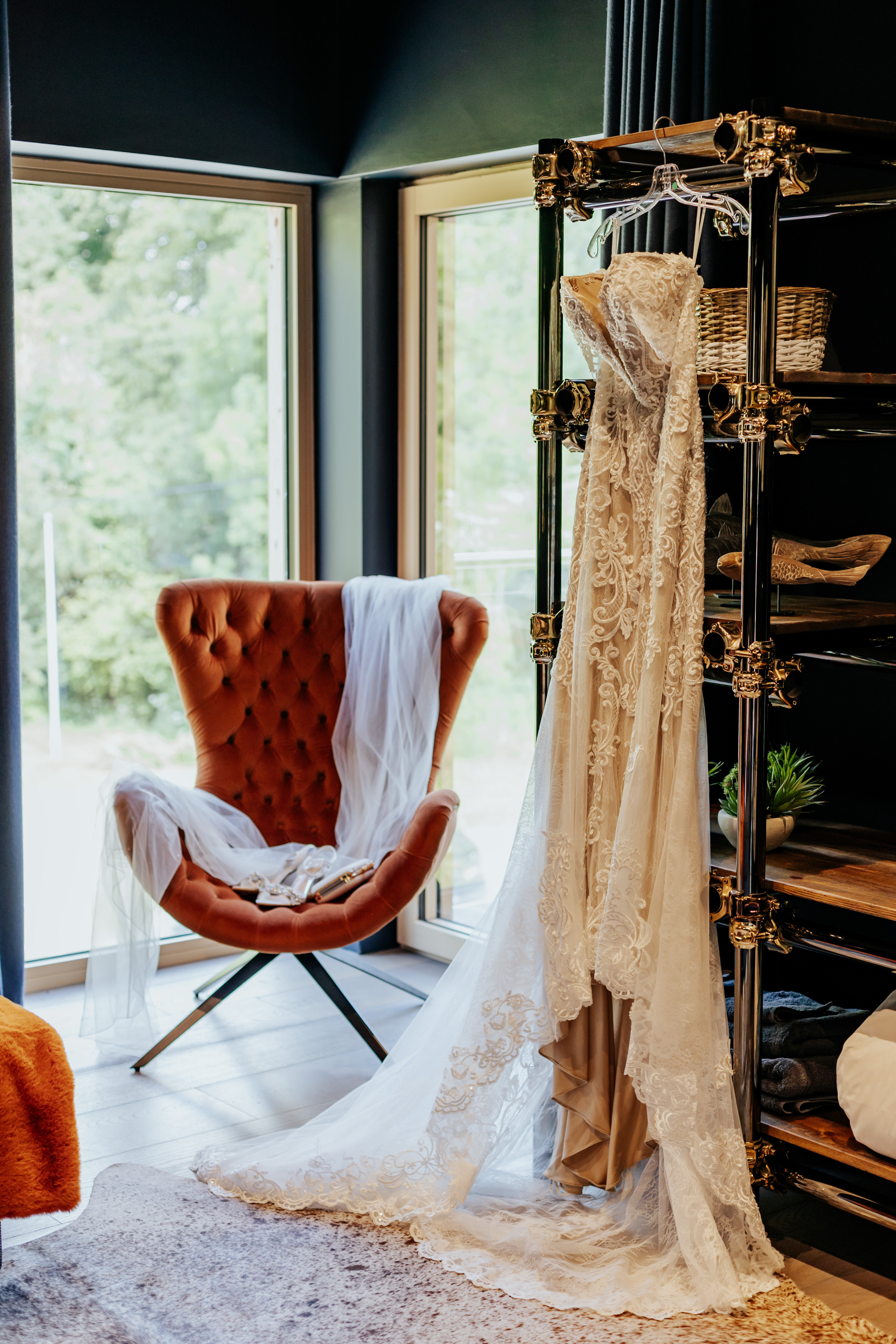 Wedding dress hanging from a bookshelf while a veil is draped over a retro chair