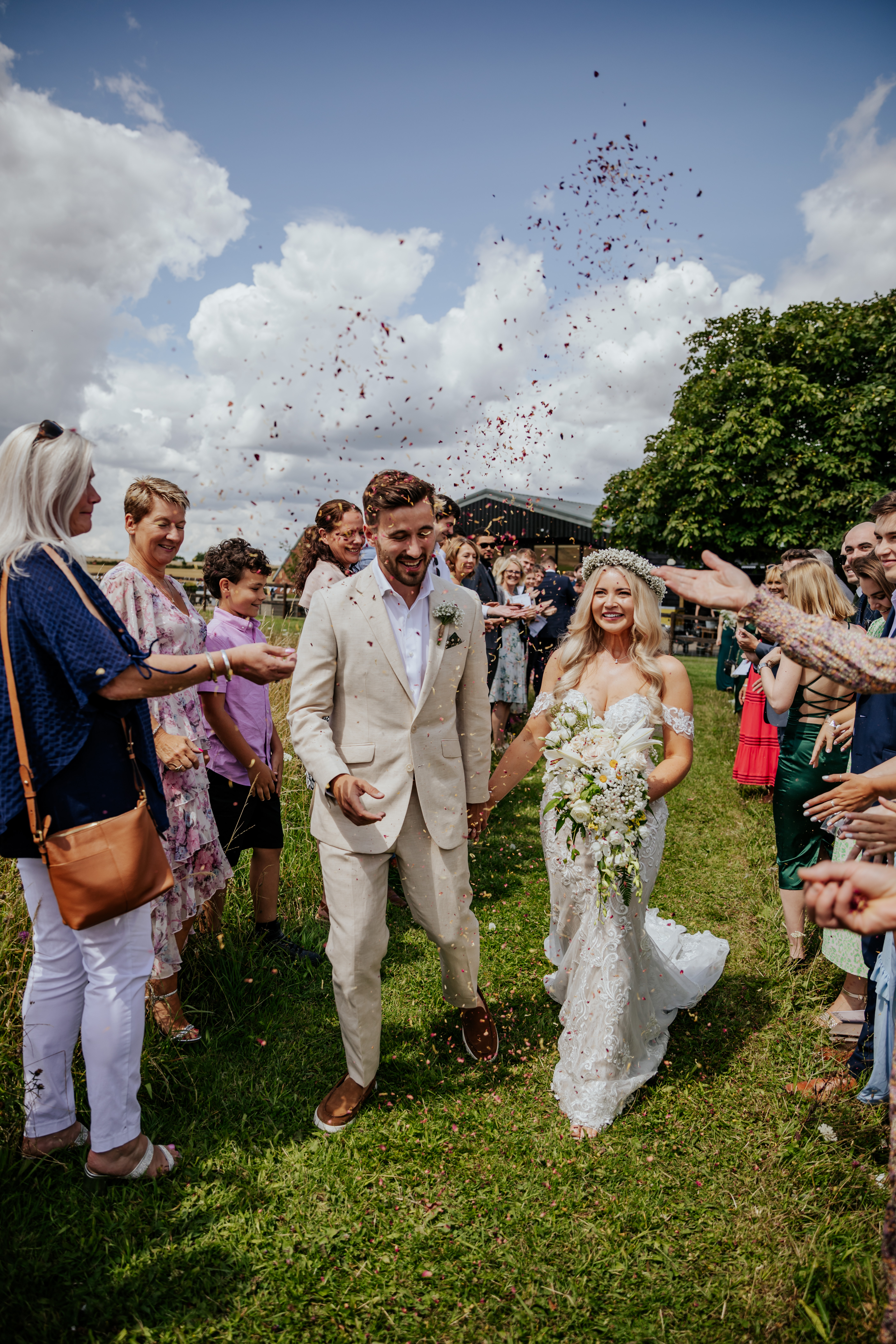 Bride and groom walk through a confetti tunnel with Wellington Barn in the background